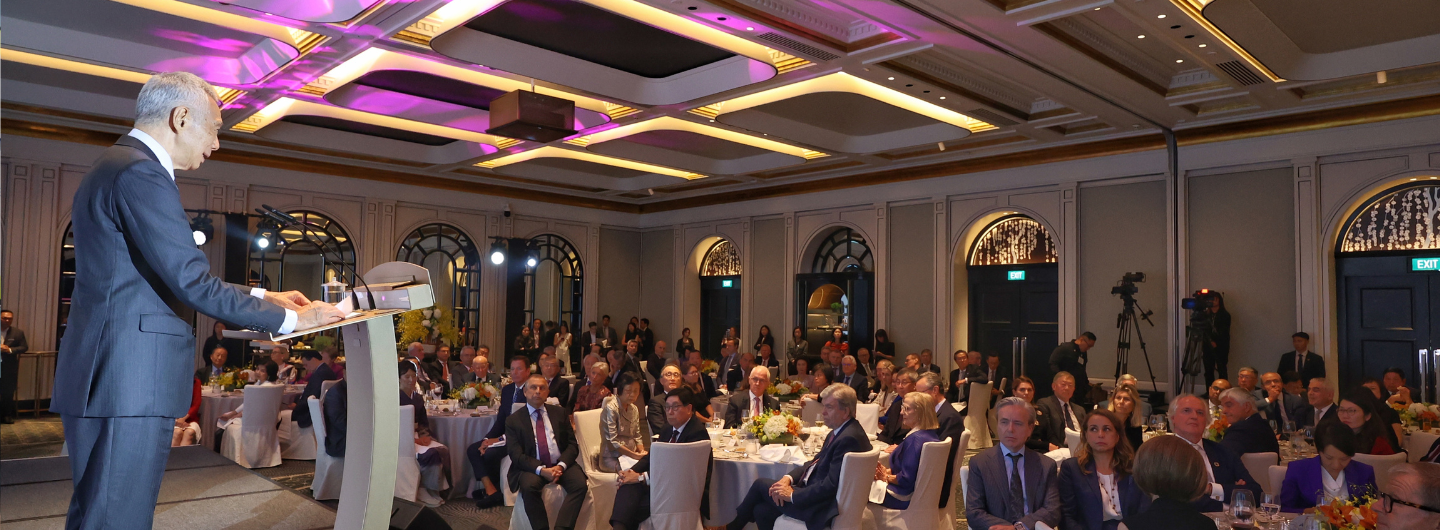 SM Lee at podium addresses a banquet audience in a grand ballroom with purple-lit ceiling.